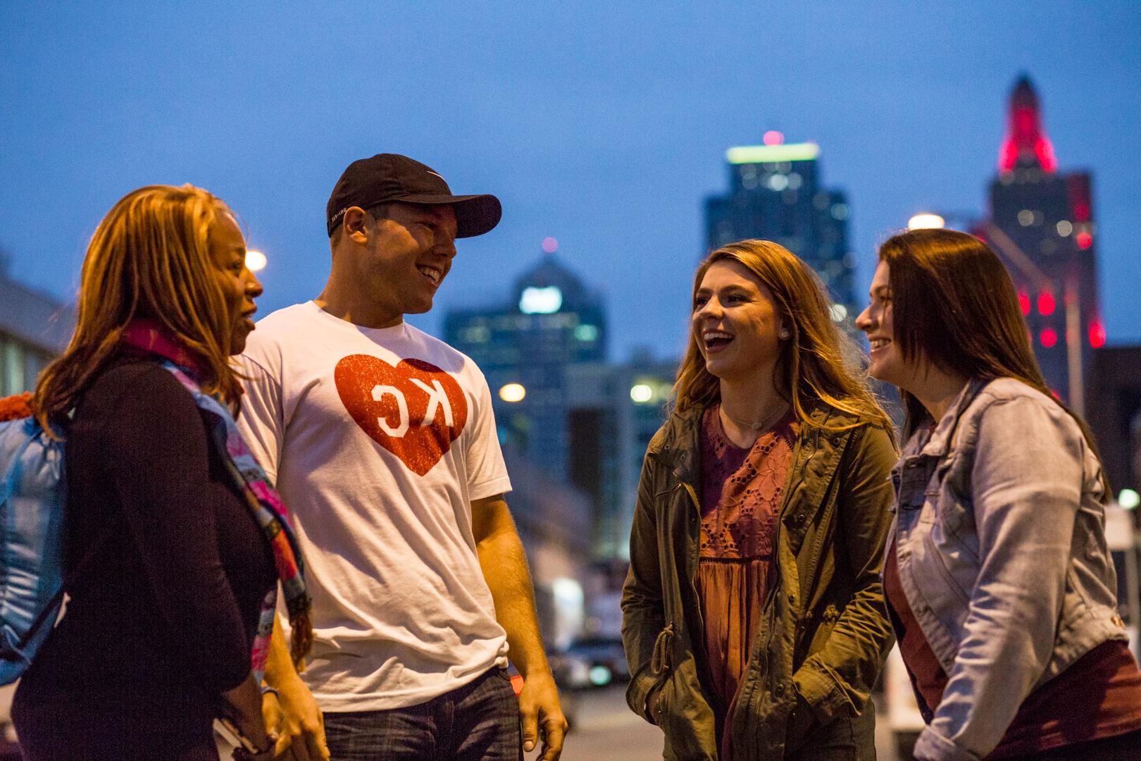 一群UMKC学生在十字路口地区的第一个星期五外出时，在堪萨斯城的天际线前有说有笑.